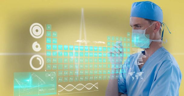 Periodic table and medical data processing over thoughtful male surgeon wearing face mask. medical research and technology concept - Фото, зображення