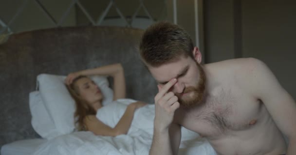 Πορτρέτο του καταθλιπτικού κοκκινομάλλη με τα γένια που ανησυχεί για τα προβλήματα στο κρεβάτι στο θολό φόντο της απογοητευμένης ξανθιάς γυναίκας που γυρίζει πίσω σε αυτόν. - Πλάνα, βίντεο