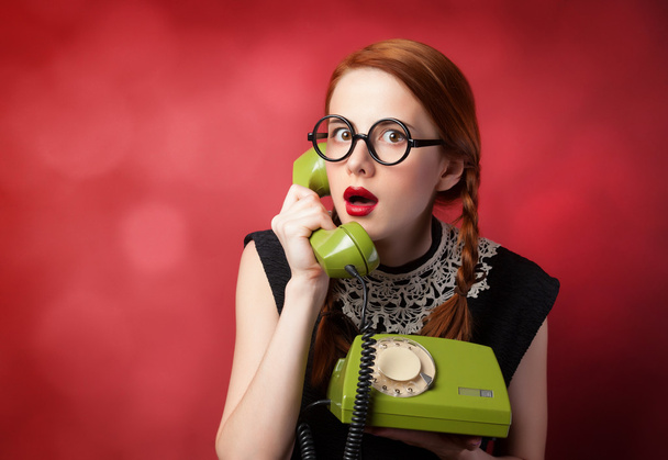 roodharige meisje met groene telefoon op rode achtergrond. - Foto, afbeelding