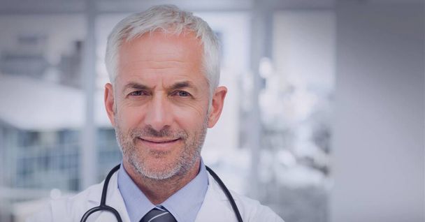 Portrait of caucasian senior male doctor against hospital in background. healthcare and medical professionalism concept - Foto, afbeelding