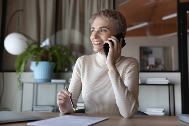 Smiling businesswoman talk on smartphone in office - Zdjęcie, obraz