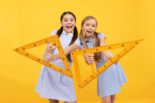 Happy school age kids hold triangular rulers yellow background, geometry. - Foto, imagen