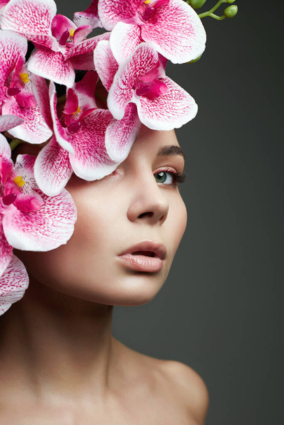 Kobieta i kwiaty. Piękny portret dziewczyny z kwiatem storczyka. Czysta skóra Twarz, pielęgnacja - Zdjęcie, obraz