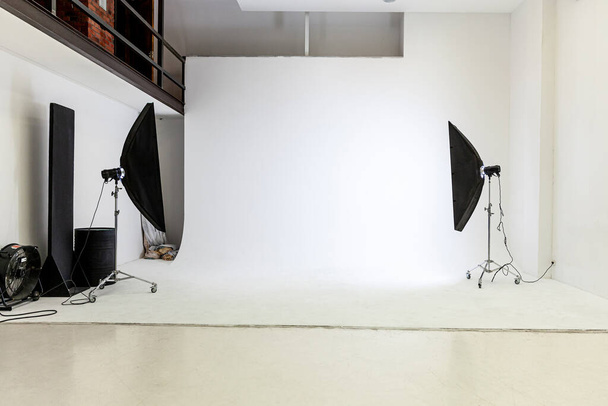 Empty photo studio with lighting equipment. Photographer workplace interior with professional tool set gear. Flash light, white background scenes ready for studio shooting. Modern photographer studio - Photo, Image