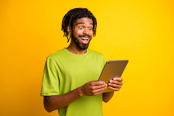 Photo of young man use modern device tablet read surprised excited news information isolated over yellow color background - Valokuva, kuva
