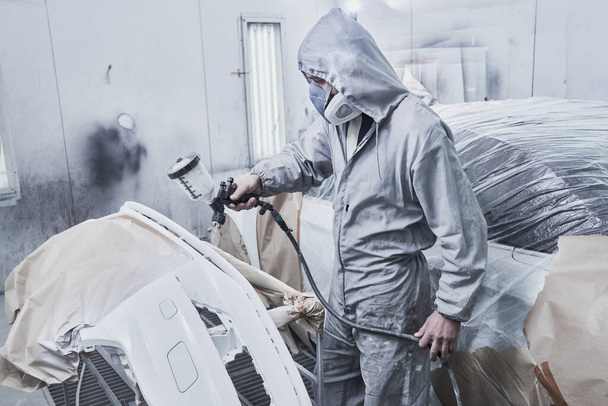 Car painting and automobile repair service. Auto mechanic in white overalls paints car with airbrush pulverizer in paint chambe - Foto, Imagem