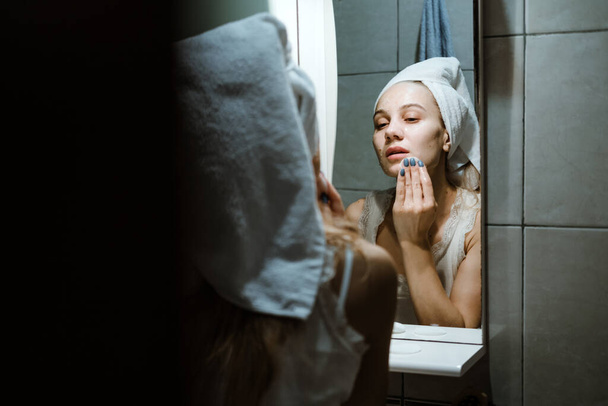 Użyj myć twarz maski, przy użyciu zdejmowanej maski poprawnie. Młoda kobieta w ręczniku na głowie umyć twarz po zdjęciu maski w łazience. - Zdjęcie, obraz