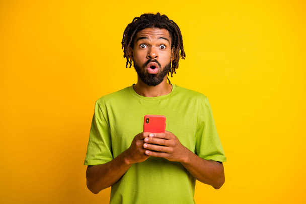 Photo of astonished dark skin guy impressed smartphone blogger novelty isolated on bright yellow color background - Foto, Bild