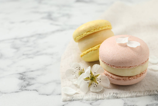 Delicious colorful macarons and flowers on white marble table. Space for text - Fotoğraf, Görsel