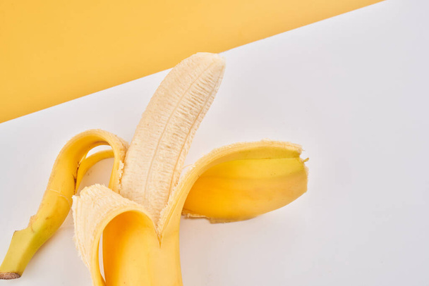Half peeled banana on yellow white background with copy space - Foto, Imagen