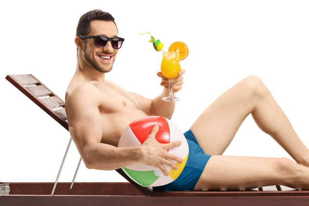 Man in swimming suit holding an inflatable ball and a cocktail isolated on white background - Fotó, kép