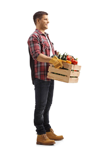 Full length shot of a farmer carrying a crate with vegetables and smiling isolated on white background - Fotó, kép