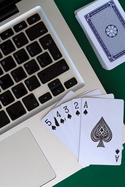 online poker hry. černý rovný záblesk rýčů s laptopem a kostkami na zelené. karty s modrým balíčkem na stole. kombinace karet na zeleném pozadí kasina s kopírovacím prostorem. vertikální. pohled shora - Fotografie, Obrázek
