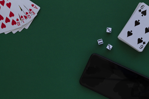 オンラインポーカーゲーム。カジノでダイスと電話で赤いロイヤルフラッシュ。緑のテーブルの上に青いデッキでトランプ。グリーンカジノのデスクの背景にあるカードとコピースペースの組み合わせです。トップビュー - 写真・画像