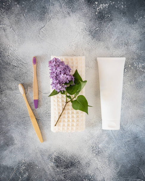 Natural, dental hygiene composition with toothbrushes, tube with toothpaste and fresh sprig of lilac on a white towel on a blue textured background with copy space. Eco friendly toothbrushing concept - Photo, image