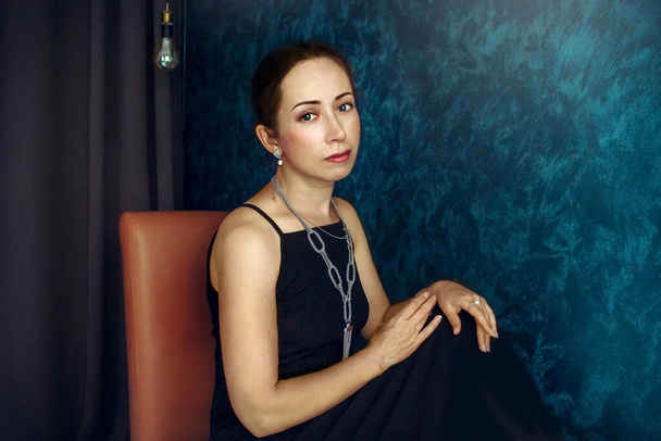 Portret van een vrouw in een zwarte jurk in een kamer met een donkerblauwe muur gestileerd als een olieverfschilderij - Foto, afbeelding
