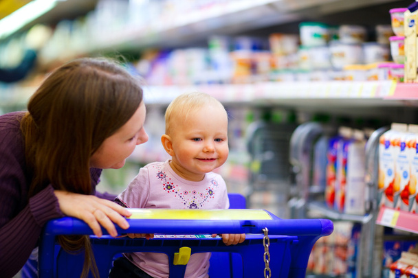 Young mother with baby daughter shopping in supermarket - Foto, Imagem