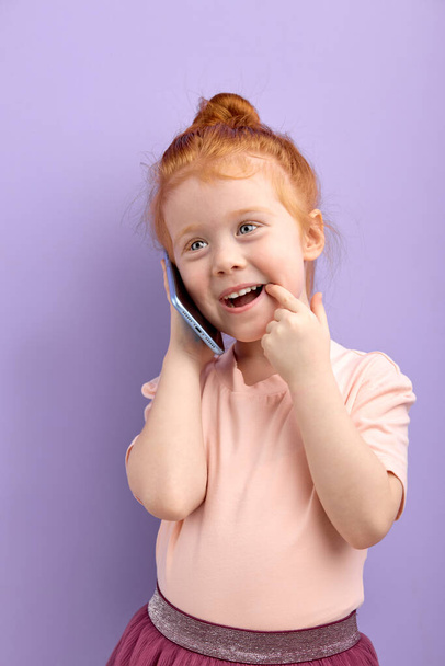 little redhead kid girl talking on phone indoors. concept of addiction of children and gadgets - Foto, afbeelding