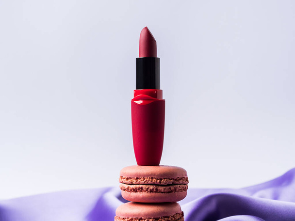 Rouge à lèvres rouge et macarons roses sur fond de tissu de soie violet - Photo, image