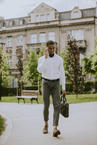 Bello giovane uomo d'affari afroamericano che utilizza un telefono cellulare su una strada - Foto, immagini