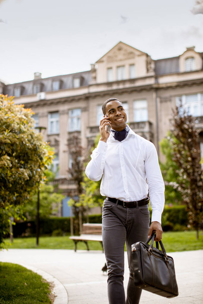 Joven empresario afroamericano guapo usando un teléfono móvil en una calle - Foto, imagen