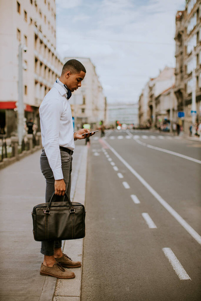 Jóképű afro-amerikai üzletember, aki mobiltelefont használ, miközben egy taxira vár, egy taxira vár az utcán. - Fotó, kép