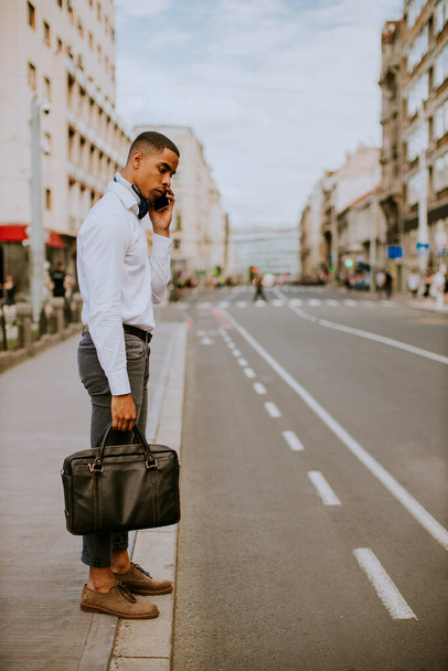 Handsome young African American businessman using a mobile phone while waitng for a taxi waitng a taxi on a street - Foto, immagini