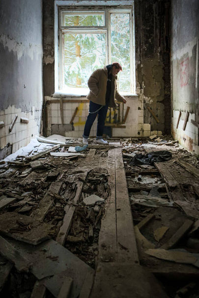 The young man with pink blonde hair in fluffy coat and black hoodie standing near the window without glass in old ruin abandoned urban building - Foto, Bild