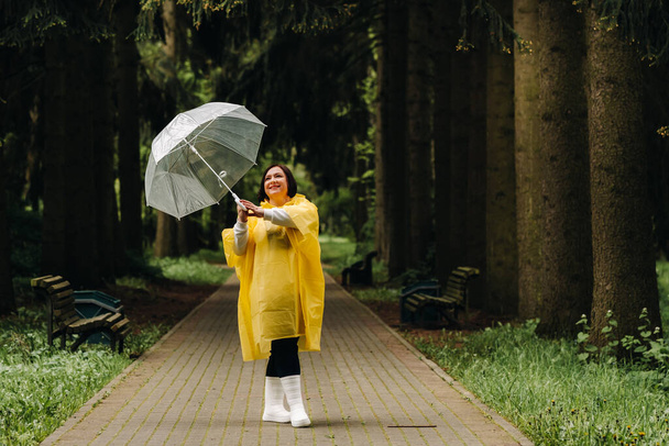 una mujer con un impermeable amarillo y un paraguas pasea por el parque y el jardín en verano. - Foto, Imagen