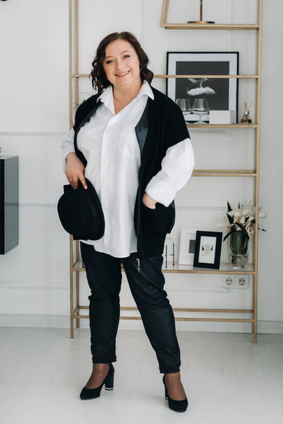 A businesswoman in a white shirt and trousers is standing with a hat in her hands standing in the office. - Foto, immagini