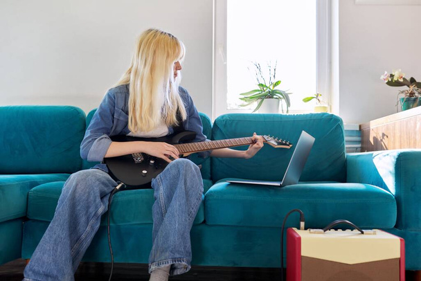 Hipster teenager girl playing electric guitar looking at laptop monitor - Фото, изображение