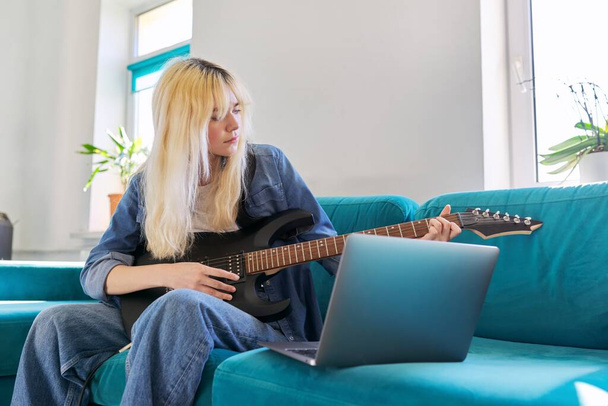 Hipster teenager girl playing electric guitar looking at laptop monitor - Foto, imagen