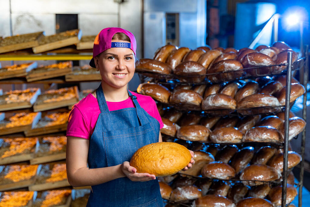 Fresh tasty bread with cheerful baker. Adorable female baker showing fresh bun. - Photo, Image