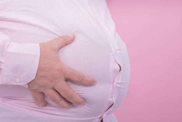 Fat man hand holding his big belly on a pink background: τυπική φωτογραφία για κοιλιά μπύρας: επιλεκτική εστίαση - Φωτογραφία, εικόνα