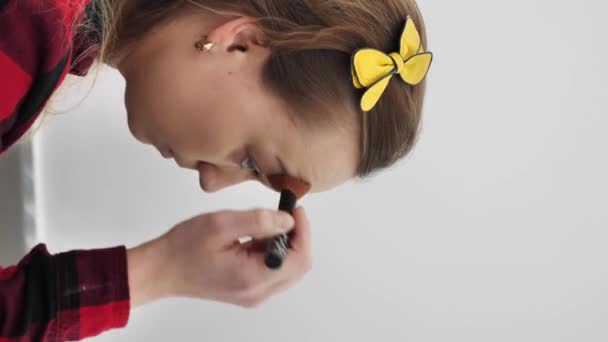 függőleges videó. A lány port alkalmaz egy ecsettel az arcán. - Felvétel, videó