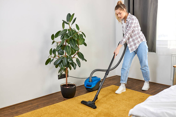 Woman in casual wear vacuum cleaning yellow carpet, tidying white modern living room. Home, housekeeping concept - Foto, imagen