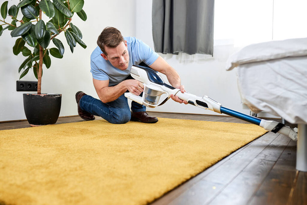 man cleaning floor with vacuum cleaner in modern white living room. Concept of easy cleaning with modern new vacuum cleaner - Fotografie, Obrázek