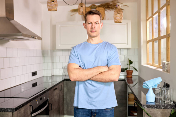Portrait Of Confident Housekeeping Man Standing At Kitchen Posing At Camera With Arms Folded - Fotografie, Obrázek