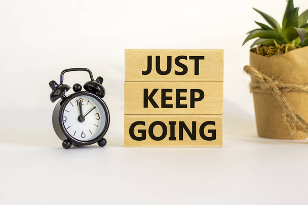 Just keep going symbol. Wooden blocks with words 'Just keep going'. Beautiful white background, black alarm clock, house plant. Business, just keep going concept, copy space. - Photo, image