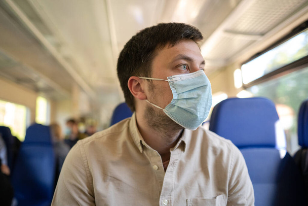 Mit öffentlichen Verkehrsmitteln sicher reisen. Zugpassagiere mit Schutzmaske sitzen auf einem Sitz mit sozialem Abstand im Eisenbahnwaggon, neue Norm. Reisen während der Coronavirus-Pandemie - Foto, Bild