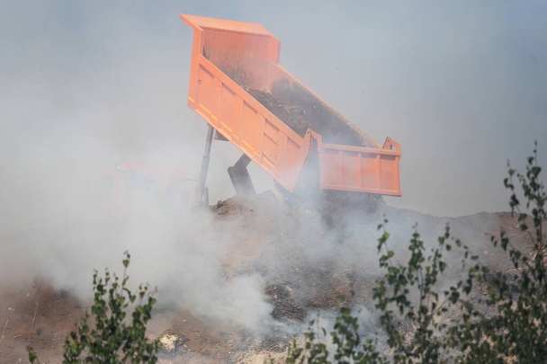 Ένα φορτηγό πετάει τόνους σκουπιδιών σε μια χωματερή. τοξικός καπνός και νέφος σε χώρους υγειονομικής ταφής επιβλαβών αποβλήτων. περιβαλλοντική καταστροφή. να σιγοκαίει σκουπίδια σε χωματερή - Φωτογραφία, εικόνα