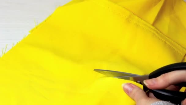 Mulheres caucasianas mãos cortando tecido amarelo brilhante com a tesoura sobre fundo mesa de madeira luz - Filmagem, Vídeo