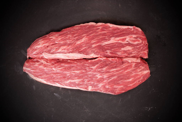 Rauwe biefstuk. Sirloin Beef Steaks, bovenaanzicht. Veel Raw Striploin Steaks van Marbled Beef op zwarte achtergrond. Een groep Black Angus Beefsteaks. Rauwe Sirloin Snijwonden. Niet gekookte eersteklas biefstuk. - Foto, afbeelding