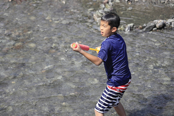 Japanese boy playing in the river with water gun (fifth grade at elementary school) - Photo, Image