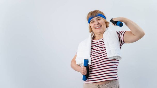 An elderly woman with a blue bandage on her head trains with dumbbells on a white background - Foto, immagini