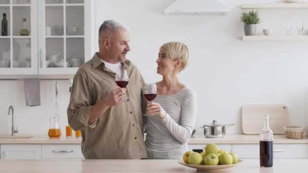 Ώριμο ζευγάρι πίνοντας κόκκινο κρασί και ψήσιμο στην κουζίνα - Πλάνα, βίντεο