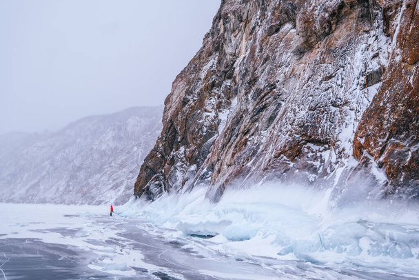 Female traveler on frozen sea near large rock. Winter landscape - Фото, изображение