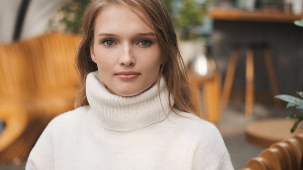 Menina bonita vestida com suéter branco acolhedor olhando atentamente na câmera descansando ao ar livre - Foto, Imagem