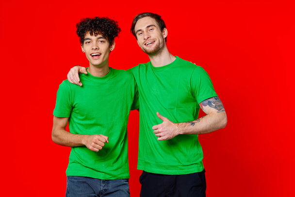 Двоє чоловіків зелені футболки охоплюють емоції дружби червоний фон
 - Фото, зображення
