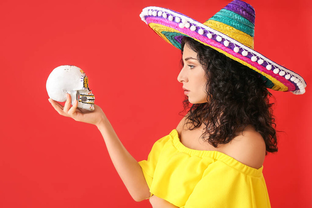 Beautiful woman in sombrero hat with skull on color background - Photo, Image